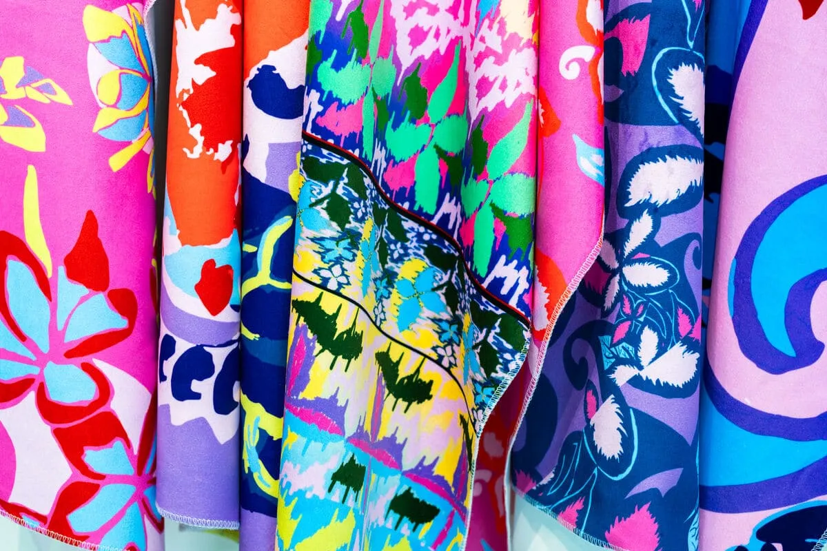 Several brightly coloured, silk fabrics covered in different floral patterns. They are hung up and folded around each other.