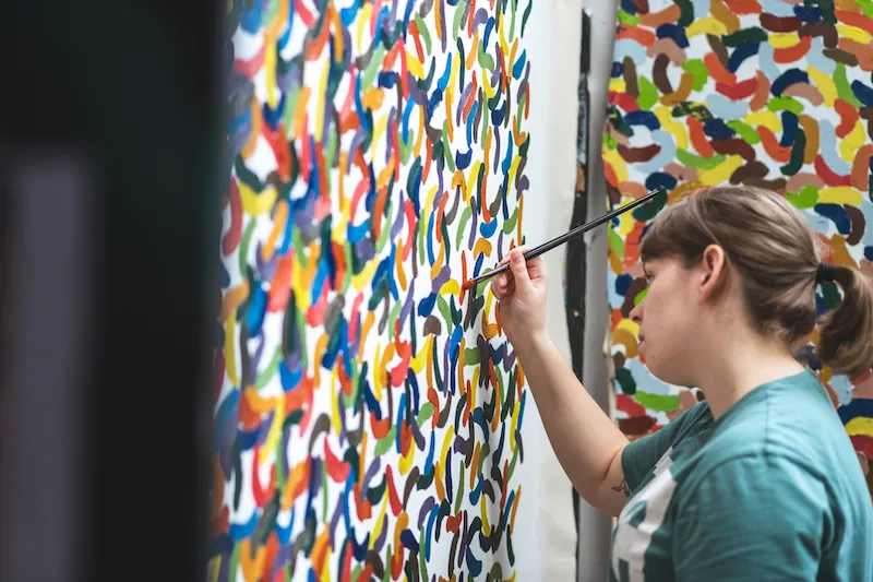 A student is completing her painting, which depicts many different colours in single brush strokes