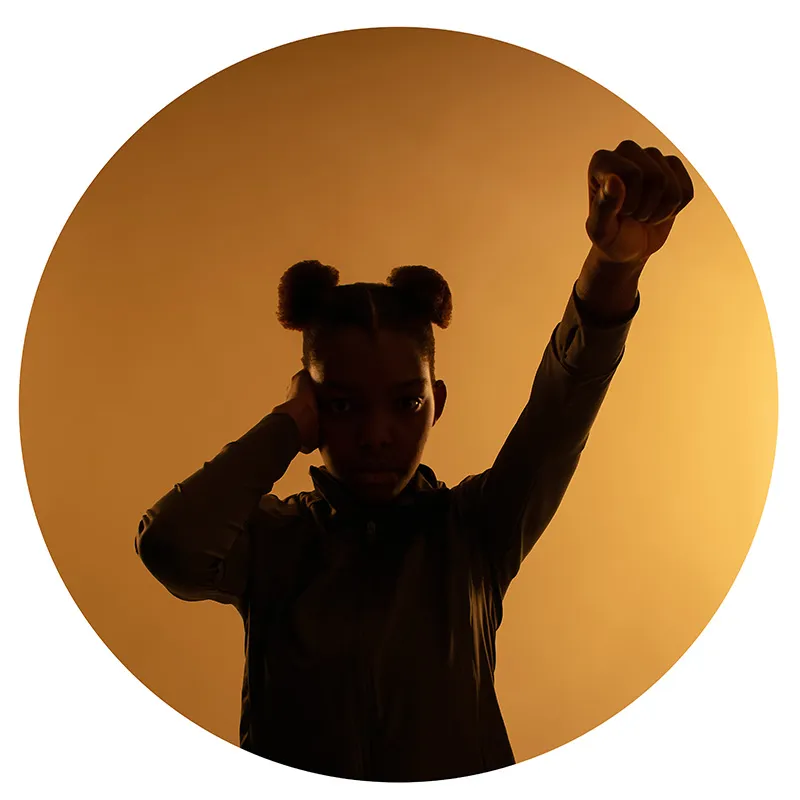 A girl with her fist raised silhouetted against a golden background