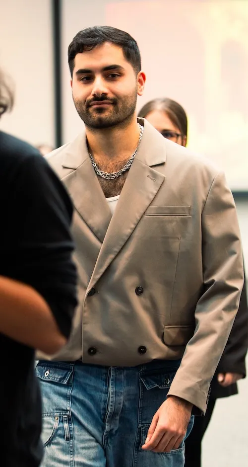 UCA alumni Zeshaan Iqbal walking, wearing a grey double breasted blazer and jeans