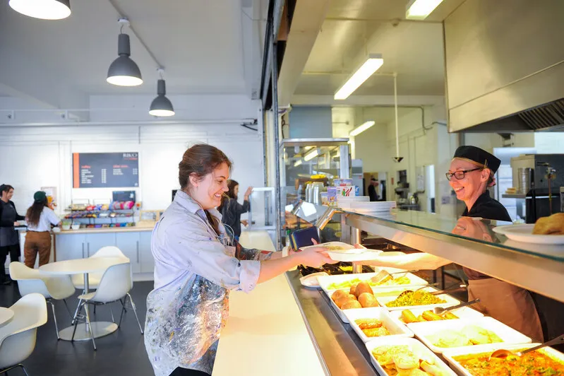 Image shows a student getting served a hot meal by staff at a UCA canteen