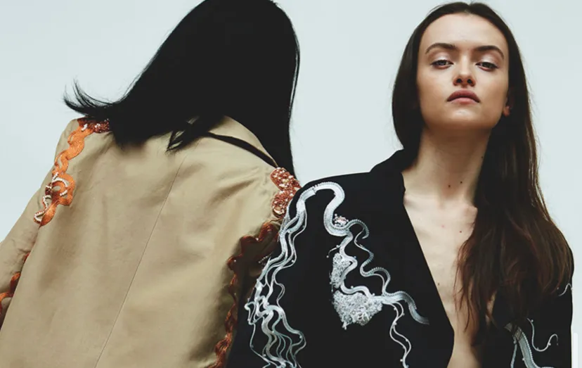 Two models dressed in embroidered tailoring, one facing us, one facing away