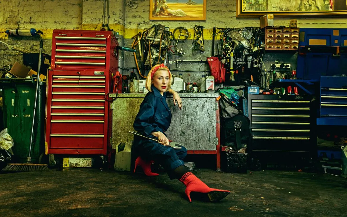 A female-presenting mechanic wearing red high-heel boots in a car garage. Artwork by Fashion Photography student, Mark Francke