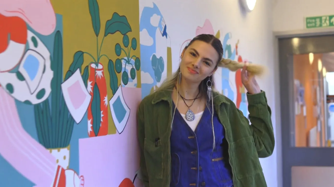 Student smiling, leaning on a wall mural