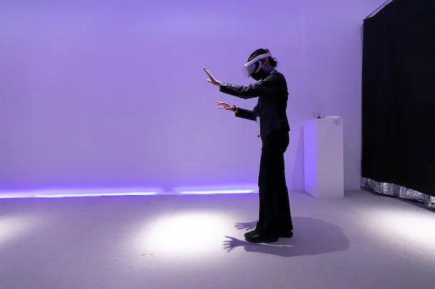 A person stands in a purple lit room with a VR headset on