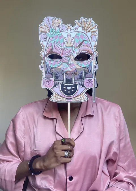 A picture of Promise Oladimeji, wearing a pink shirt, and holding up an intricate mask