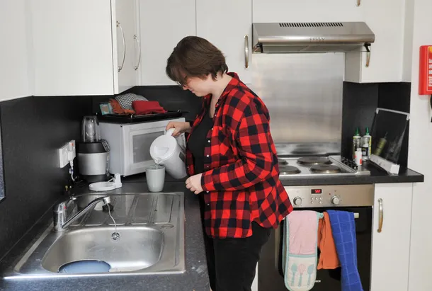 A student is making a hot drink, pouring hot water from a kettle