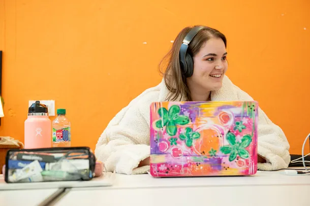 A student sits in front of her laptop against a bright yellow background