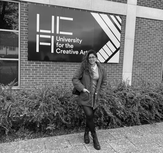 International student Sasha Miranda, in a red coat, stands in front of some UCA signage at the Epsom campus