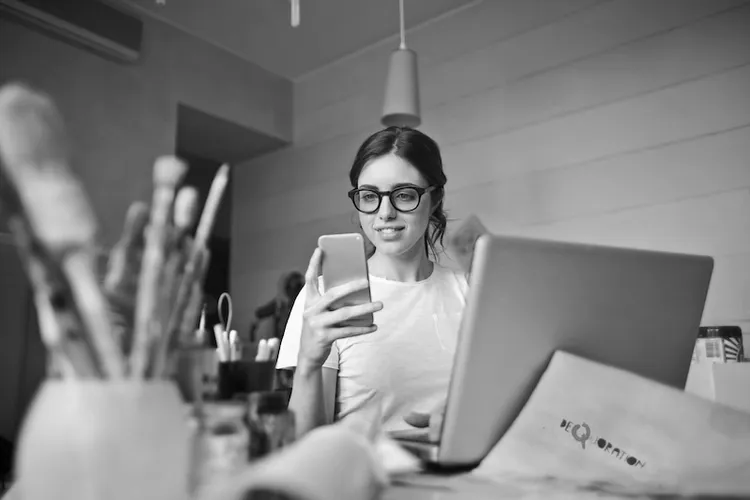 A girl in front of her laptop and art supplies on her phone