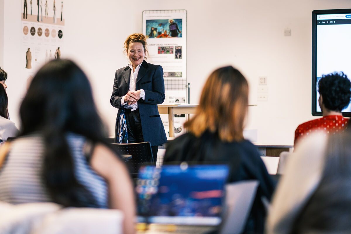 A lecturer standing in front of a small seminar group, there are 2 people in the foreground on laptops.